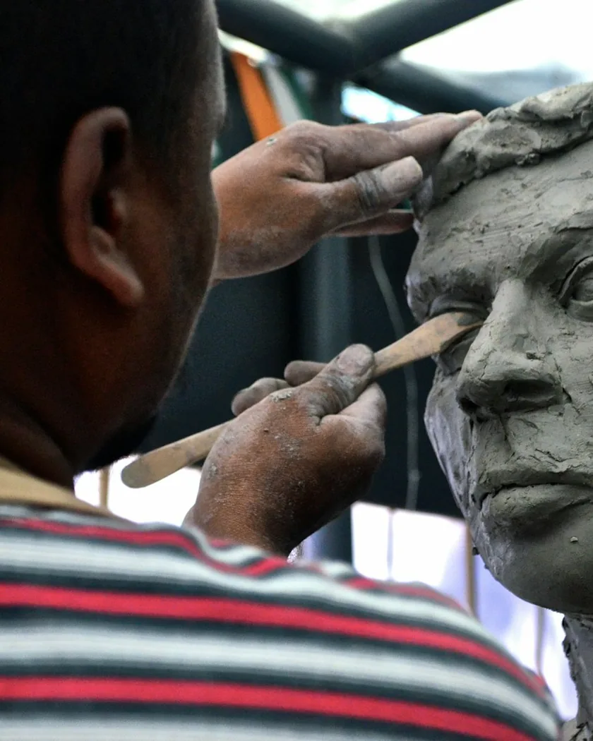 Manos trabajando con una esteca sobre la zona del ojo de un retrato modelado en arcilla.